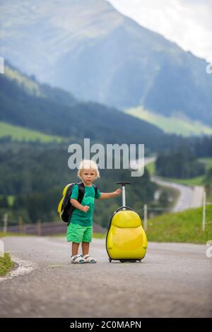 Kleines Kind, Junge mit Rucksäcken und Koffer, Reisen auf der Straße zu malerischen Bergen, Sommerzeit Stockfoto