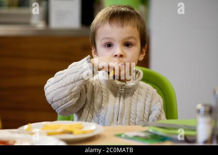 Kleiner kleiner kleiner Junge, der Junk Food im Restaurant isst Stockfoto