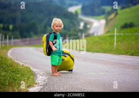 Kleines Kind, Junge mit Rucksäcken und Koffer, Reisen auf der Straße zu malerischen Bergen, Sommerzeit Stockfoto