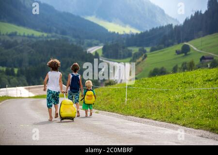 Kleine Kinder, Junge Brüder mit Rucksäcken und Koffer, reisen auf der Straße zu malerischen Bergen Stockfoto