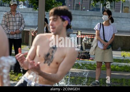 Moskau, Russland. 11. Juni 2020 EINE Frau mit Gesichtsmaske kümmert sich um Menschen, die in einem Fußgängerbrunnen im Muzeon-Park auf Krymskaya-Ufer während abnormer Hitze in Moskau, Russland baden Stockfoto