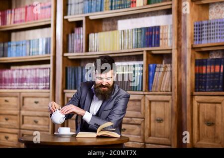 Lachen, Entspannen, Vergnügen, Freizeit, Hobby-Konzept. Happy man sitzt im Vintage-Interieur und genießt entspanntes Lesen. Bärtiger Mann in formeller Kleidung besucht Bibliothek. Reifer Mann mit lächelndem Gesicht hat Tee. Stockfoto