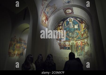 Besucher vor dem mittelalterlichen romanischen Fresko, das vor 1123 von der Kirche Sant Climent de Taüll in der Gegend von Vall de Boí in Alta Ribagorça in Katalonien, Spanien, fertig gestellt wurde, jetzt im Nationalen Kunstmuseum von Katalonien (Museu Nacional d'Art de Catalunya) in Barcelona, Katalonien, Spanien. Jesus Christus in Majestät ist in der Apsis dargestellt. Stockfoto