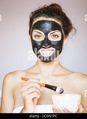 Junge Frau, die eine Maske für das Gesicht des therapeutischen schwarzen Schlamms aufwendet Stockfoto
