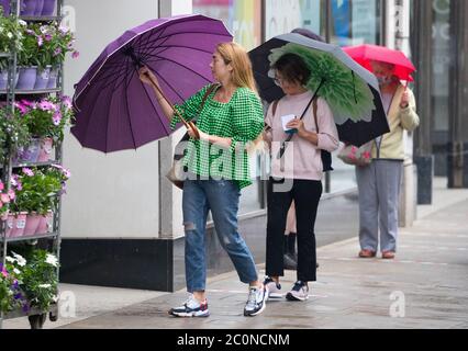 Winchester, Hampshire. Juni 2020. Wetter in Großbritannien. Besucher von Winchester erwischten in einer Regendusche. Damen mit Brollys Schlange für Marks und Spencer Food Hall. Credit Stuart Martin/Alamy Live News Stockfoto