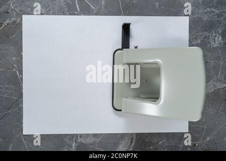 Locher auf einem weißen Blatt Papier auf einem grauen Marmortisch Stockfoto