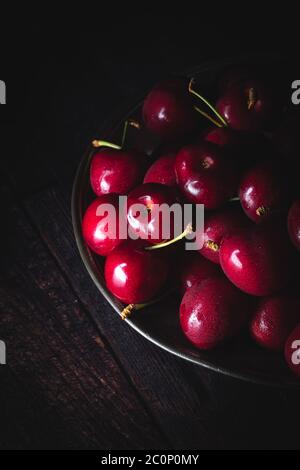 Dunkelrote Kirschen auf einem Zinnteller. Schwaches Licht, Draufsicht. Stockfoto