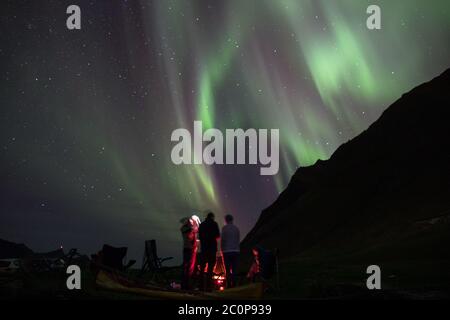 Freunde umrunden ein Lagerfeuer unter den Nordlichtern. Stockfoto