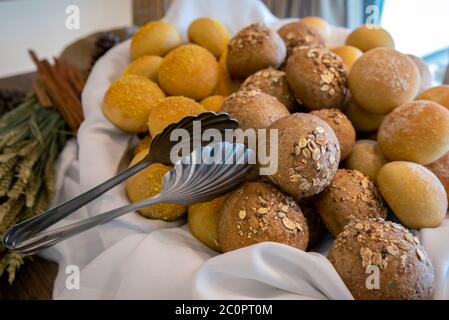 Nahaufnahme von runden verschiedenen Arten von gebackenen kleinen Broten aus verschiedenen Zutaten auf einem weißen Tuch in einem Korb mit einer Küchenzange Stockfoto