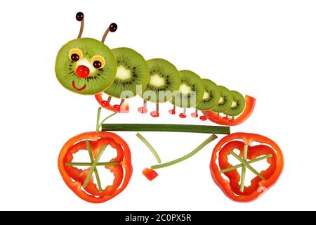 Kreatives Food-Konzept. Lustige kleine Raupe auf einem Fahrrad aus Obst und Gemüse Stockfoto