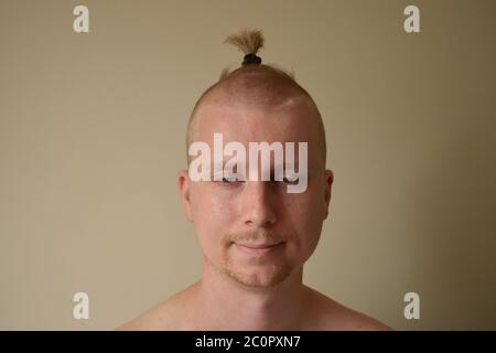 Junger Mann, der sich selbst eine schreckliche Home Haarschnitt in Lockdown hat zieht ein lustiges Gesicht mit einem Bobble in Was ist links von seinem Haar Stockfoto