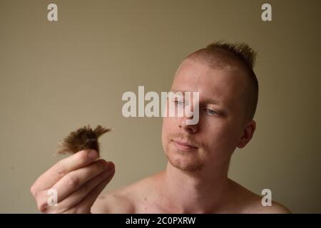 Der junge Mann schaut auf ein Haar, nachdem er sich zu Hause während des Lockdown einen schlechten Haarschnitt gegeben hat Stockfoto