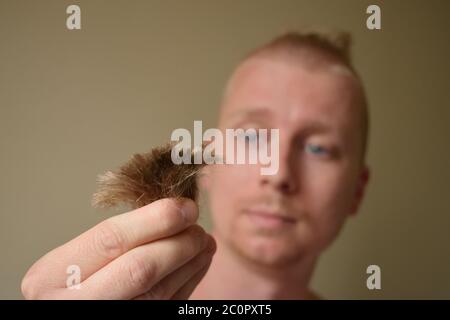 Der junge Mann schaut auf ein Haar, nachdem er sich zu Hause während des Lockdown einen schlechten Haarschnitt gegeben hat Stockfoto