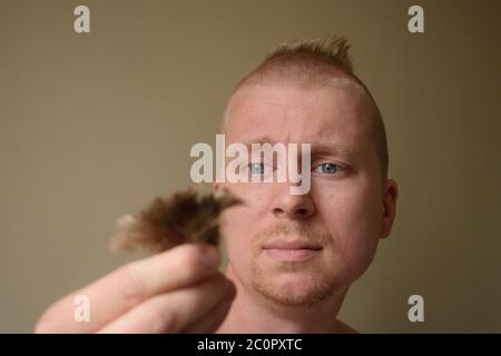 Der junge Mann schaut auf ein Haar, nachdem er sich zu Hause während des Lockdown einen schlechten Haarschnitt gegeben hat Stockfoto