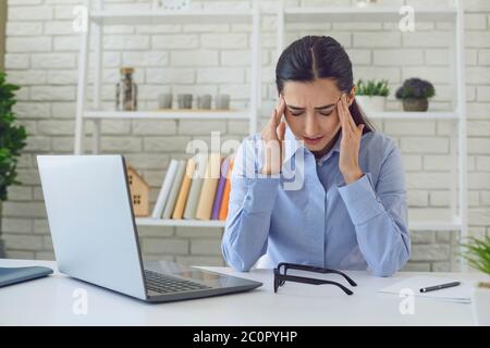 Frau mit Kopfschmerzen. Frau professionelle im Home Office mit Laptop-Computer Kopfschmerzen aufgrund von Arbeitsstress. Stockfoto