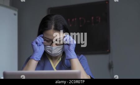 Müde Arzt entfernt Brille während eine Pause von der Arbeit auf Laptop-Computer im Büro. Überlastung während einer Pandemie Stockfoto