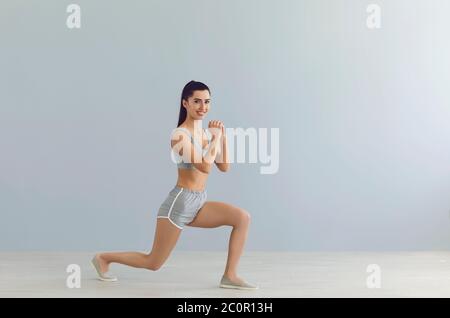 Schöne lächelnde Mädchen in Sportswear arbeiten auf grauem Hintergrund, leeren Raum. Athletic Mädchen tun Cardio-Übungen Stockfoto