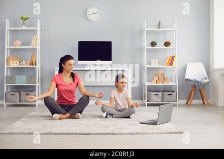 Yoga-Familie. Mutter und Tochter üben Online-Yoga-Video-Kurs haben einen Laptop sitzen auf dem Boden in einem Raum drinnen. Stockfoto