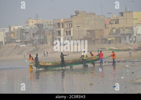 Eine Gruppe von handwerklichen Fischern, die einen Pirogue in Yoff Beach, Dakar, Senegal, schieben Stockfoto