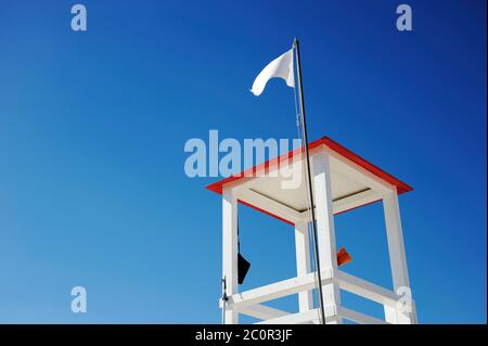 Rettungsschwimmer Holzturm am Strand gegen blauen Himmel. Megafon und andere Werkzeuge hängen vom Turm. Die weiße Fahne schwenkt auf das Dach.Platz kopieren für Stockfoto