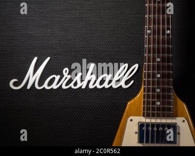 Teil des Stoffgrills eines kultigen Marshall 4 x 12 Lautsprecherschranks, mit Teil eines Halses und Korpus einer Gibson Flying V E-Gitarre, neben dem Logo. Stockfoto