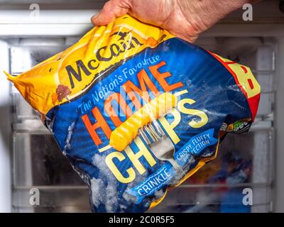 Ein Mann Hand hält eine Tasche von McCain crinkle geschnitten gefrorenen Home Chips, vor einem Gefrierschrank. Stockfoto