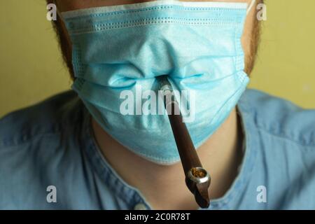 Bärtiger Mann in einer medizinischen Maske raucht eine Pfeife mit Tabak aus nächster Nähe. Stockfoto