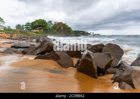 Strand mit rotem Sand und roten Felsen mit einem dramatischen Himmel in Congo Town, Monrovia, Liberia Stockfoto