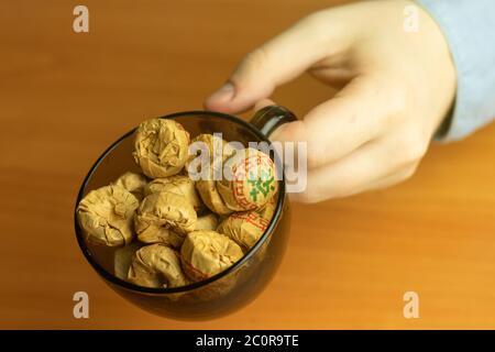 Chinesischer Puer Kräutertee in einer Packung in einer Tasse in der Hand Nahaufnahme. Stockfoto