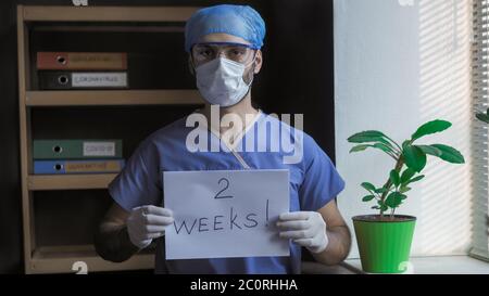 Der männliche Arzt berichtet über das Ende der Coronavirus-Quarantäne in zwei Wochen. Der Arzt in weißen Handschuhen bittet, noch zwei Wochen zu Hause zu bleiben. Pandemie Stockfoto