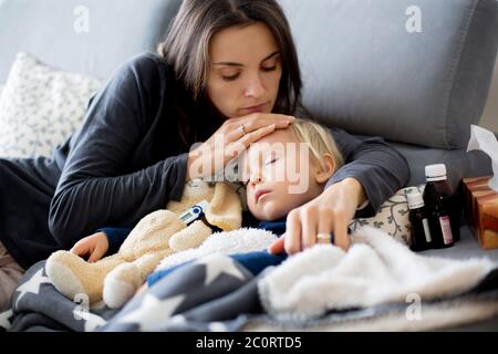 Blonde Kleinkind Junge, schlafen auf der Couch im Wohnzimmer, liegend mit Fieber, Mama auf ihn überprüfen Stockfoto