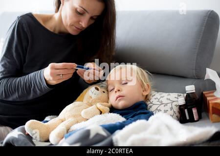 Blonde Kleinkind Junge, schlafen auf der Couch im Wohnzimmer, liegend mit Fieber, Mama auf ihn überprüfen Stockfoto