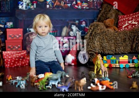 Sweet blonde Kleinkind Junge, spielen mit Kunststoff-Tiere und Dinosaurier zu Hause, weihnachtsdekoration um ihn herum Stockfoto