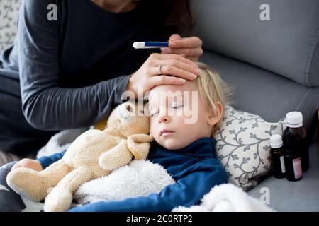 Blonde Kleinkind Junge, schlafen auf der Couch im Wohnzimmer, liegend mit Fieber, Mama auf ihn überprüfen Stockfoto