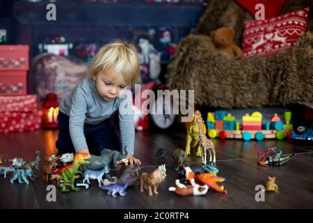 Sweet blonde Kleinkind Junge, spielen mit Kunststoff-Tiere und Dinosaurier zu Hause, weihnachtsdekoration um ihn herum Stockfoto