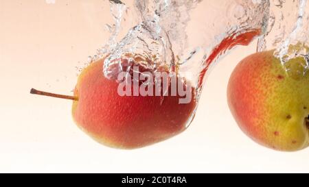 Frische Birne mit grün-roten Seiten fällt ins Wasser klopft Spritzer aus Stockfoto