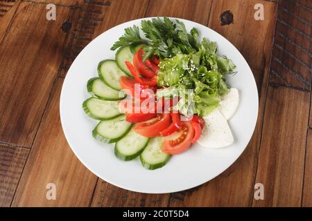 Gemüsebrühe Salat, Gurke, Tomate, Petersilie und Käse auf einem weißen Teller. Holzhintergrund. Stockfoto