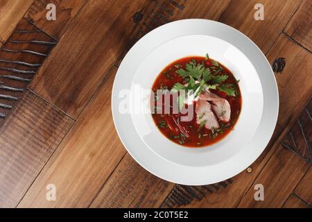 Borscht - russische und ukrainische traditionelle Suppe auf einem weißen Teller. Holzhintergrund Stockfoto