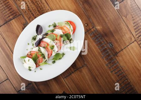Salat mit Mozzarella-Käse und Tomaten in weiß ovaler Platte. Holzhintergrund. Stockfoto