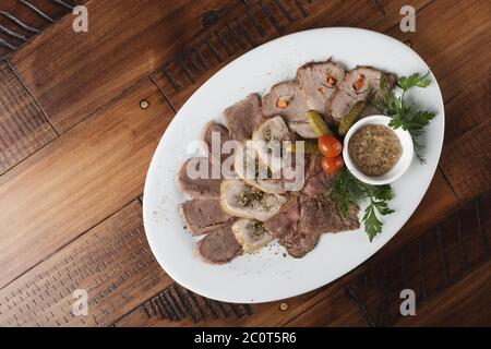 Gebratenes Roastbeef, Hühnerbrötchen, Zunge und Schweinefleisch mit Gemüse auf einem weißen ovalen Teller. Holzhintergrund. Stockfoto