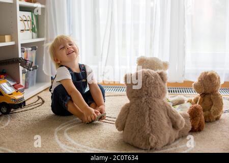 Kleiner kleiner kleiner kleiner Junge, der ein Buch zu seinen Teddybären Freunden zu Hause liest, sitzt im Wohnzimmer Stockfoto