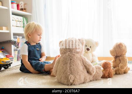 Kleiner kleiner kleiner kleiner Junge, der ein Buch zu seinen Teddybären Freunden zu Hause liest, sitzt im Wohnzimmer Stockfoto