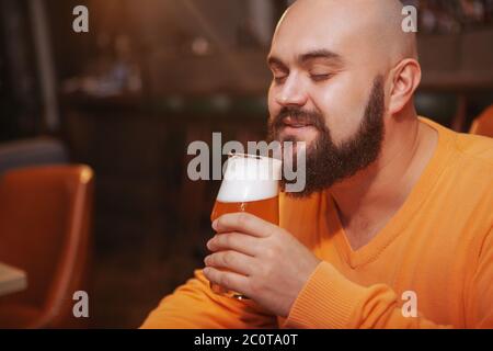 Nahaufnahme eines fröhlichen bärtigen Mannes, der lächelt und riecht nach köstlichem Bier in einem Glas Stockfoto