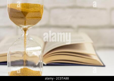 Eine Sanduhr und ein offenes Buch auf dem Tisch. Stockfoto