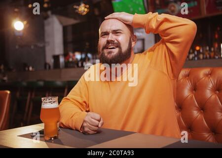 Bärtiger Mann, der Fußball im Bierkneipe beobachtet und aufgeregt aussuht Stockfoto