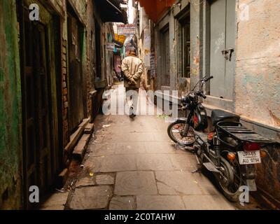 Varanasi, Uttar Pradesh, Indien - Februar 2015: Eine enge gepflasterte Gasse in der Altstadt von Benares mit einem geparkten Motorrad in einer Ecke. Stockfoto