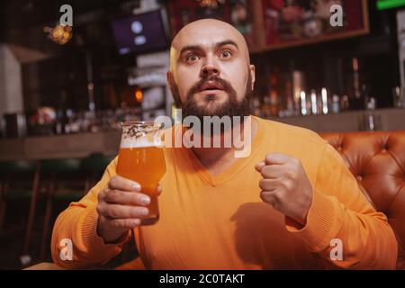 Attraktiver Mann, der Fußballspiel an der Sportbar beobachtet und Bier in der Hand hält Stockfoto