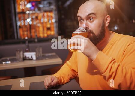 Kahler Mann, der überwältigt aussieht und im Pub leckeres Bier trinkt. Reifer Mann trinkt leckeres Bier mit Vergnügen Stockfoto