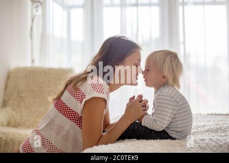 Mutter und Sohn, Kleinkind Junge, sitzen auf dem Bett, Hände halten, einander anschauen Stockfoto