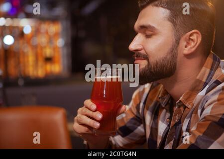 Nahaufnahme eines gutaussehenden, entspannten Mannes, der in seinem Glas nach köstlichem Bier riecht. Glücklicher Mann, der im Bierkneipe trinkt Stockfoto